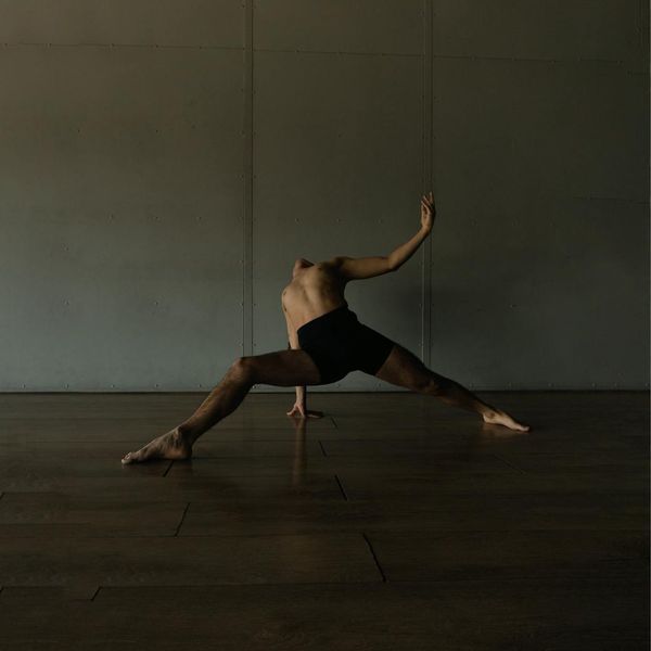 Person in a dynamic yet controlled movement pose in a minimalist studio.